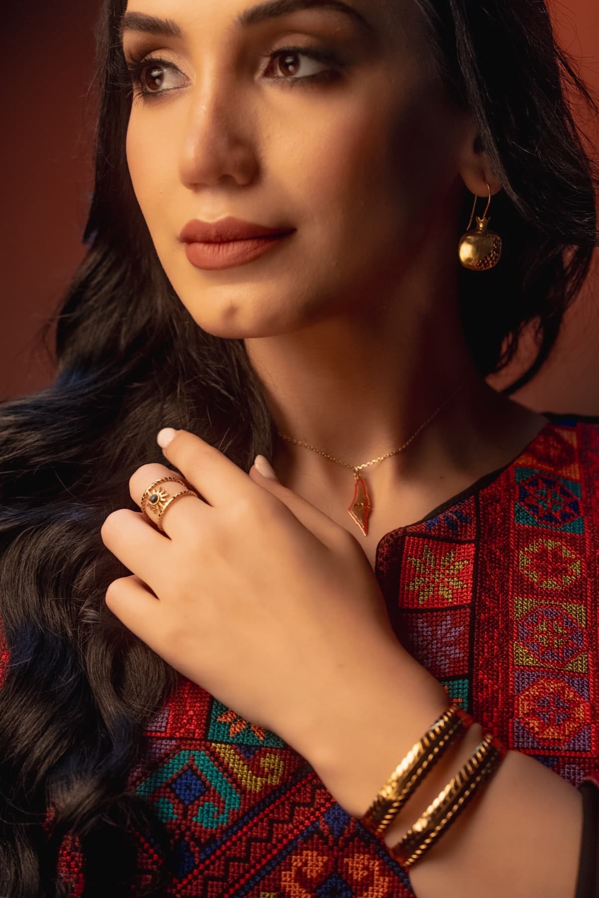 Pomegranate jewelry detail against embroidered garment