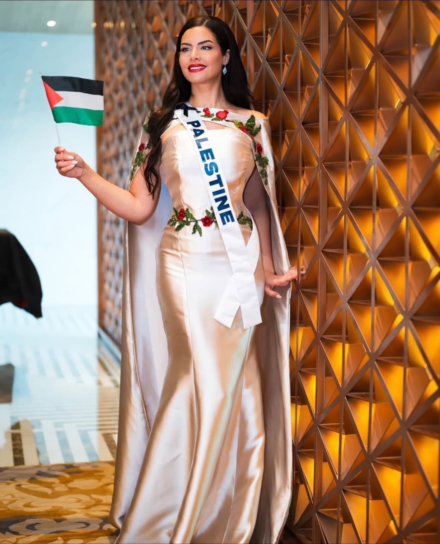 Nadeen Ayoub wearing Miss Palestine sash and holding the Palestinian flag